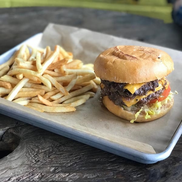A double cheeseburger with lettuce, tomato, and caramelized onions, served with a side of fries.