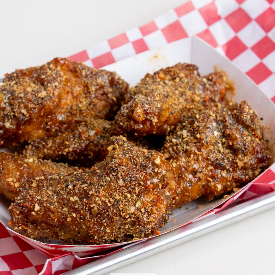 Crispy fried chicken pieces coated in coarse seasoning, served in a tray lined with red-and-white checkered paper.