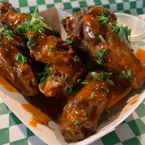 Close-up of several chicken wings coated in a glossy, reddish-brown sauce and garnished with fresh parsley.