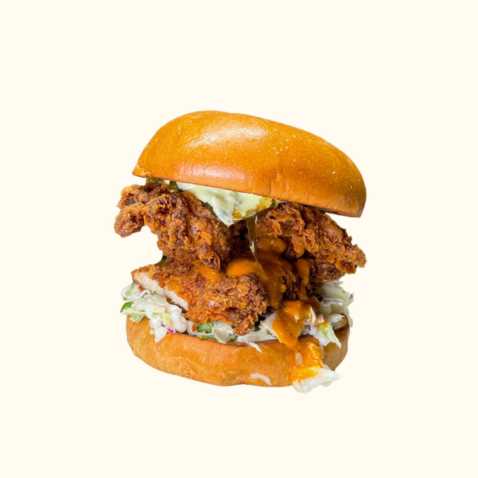Crispy fried chicken sandwich with coleslaw, melted cheese, pickles, and orange sauce on a golden brioche bun.