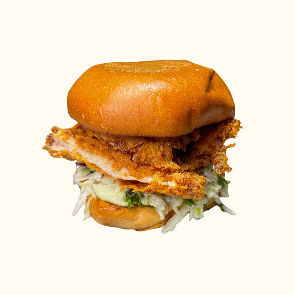 Crispy fried chicken sandwich with shredded lettuce and sauce on a glossy toasted bun.