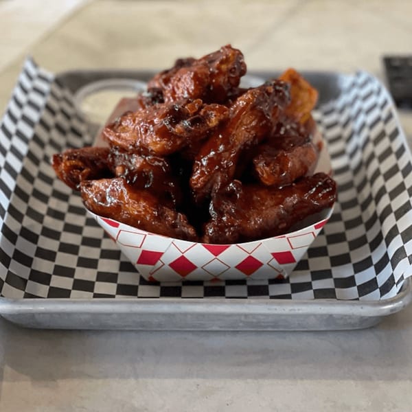 A serving of barbecue chicken wings in a paper boat on a checkered paper-lined metal tray.